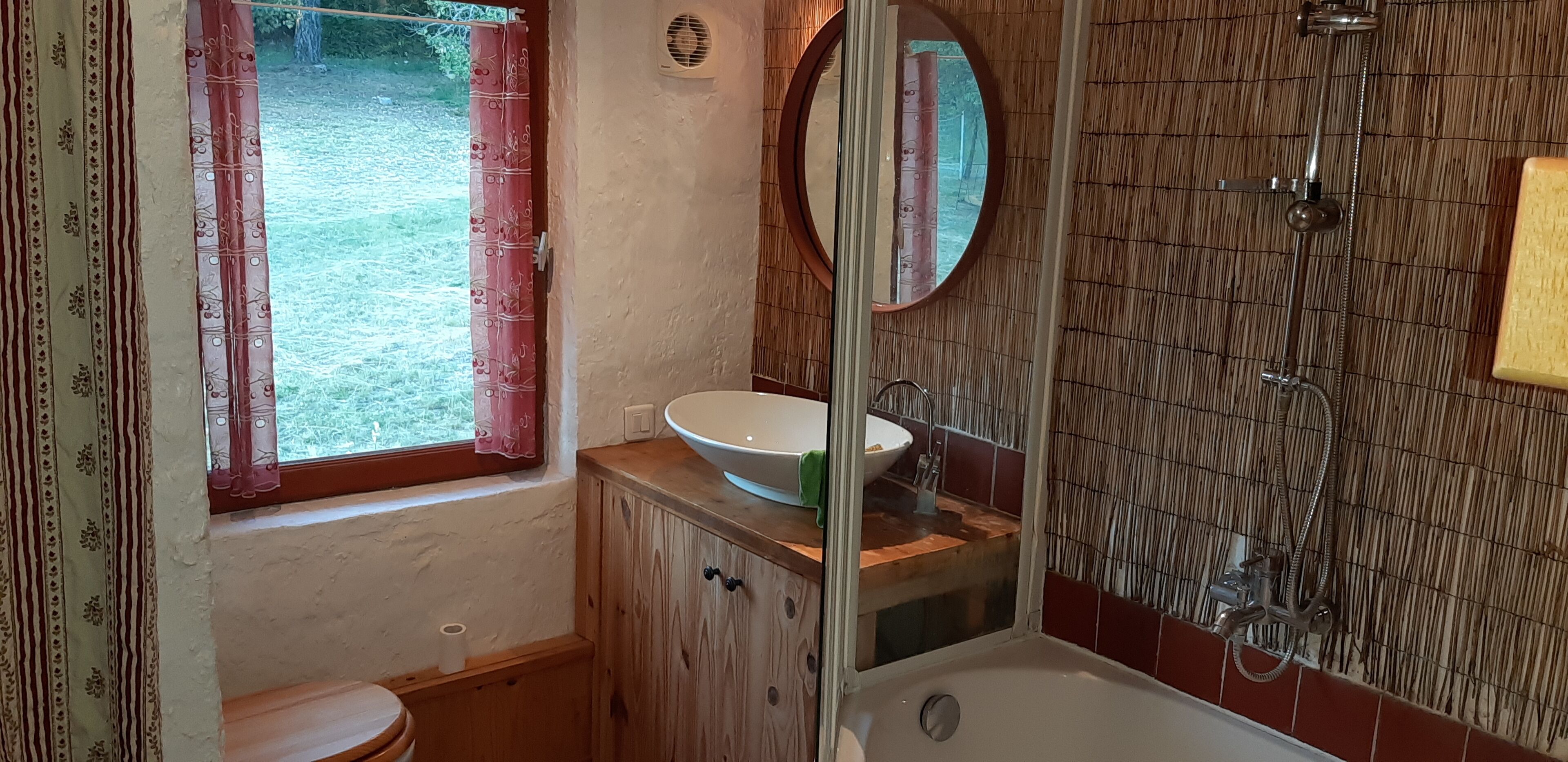 Un baño con tocador de madera, lavamanos blanco, espejo y zona de ducha.