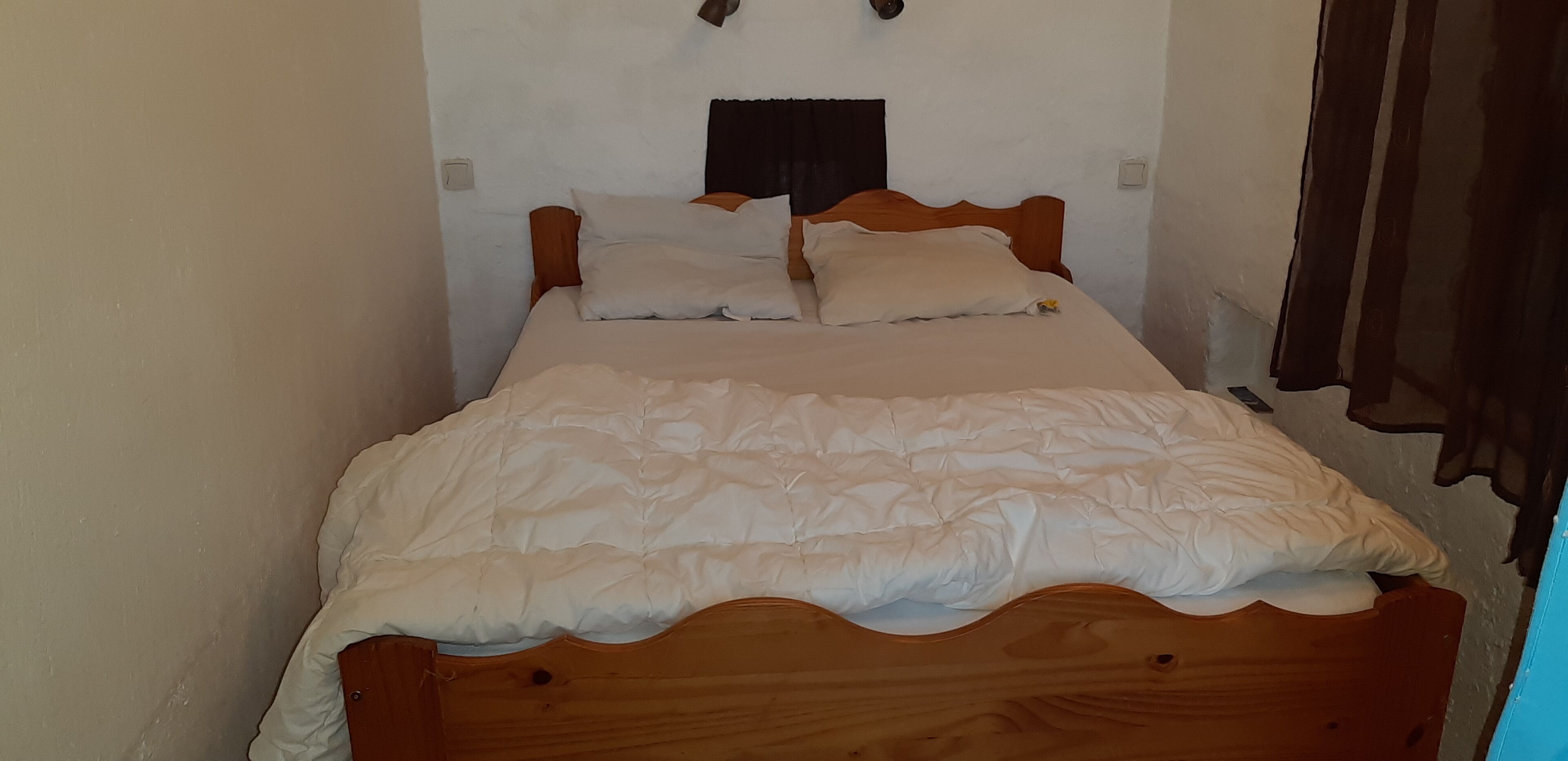 A single bed with a wooden headboard, white bedding, and a small window with a curtain.
