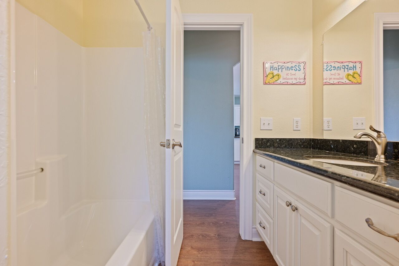 A bathroom with white cabinets, a black countertop, and a mirror. There are two signs on the wall that read "Happiness" and "Happiness."