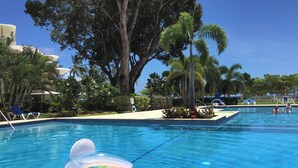 A swimming pool with two inflatable floaties, surrounded by palm trees and lounge chairs.