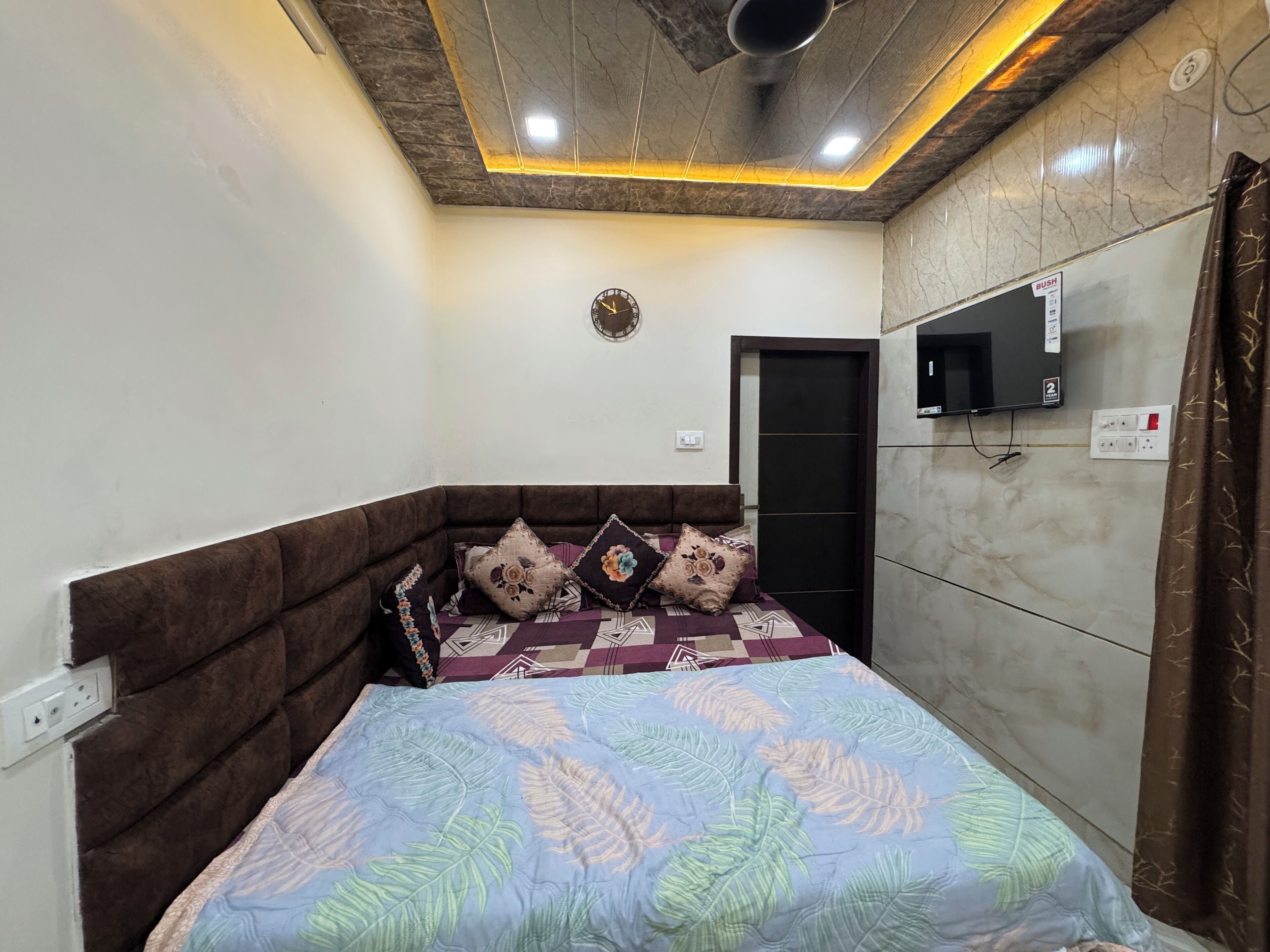 Ein Schlafzimmer mit einem Bett, einem an der Wand montierten Fernseher und einer Decke mit einer Leuchte.