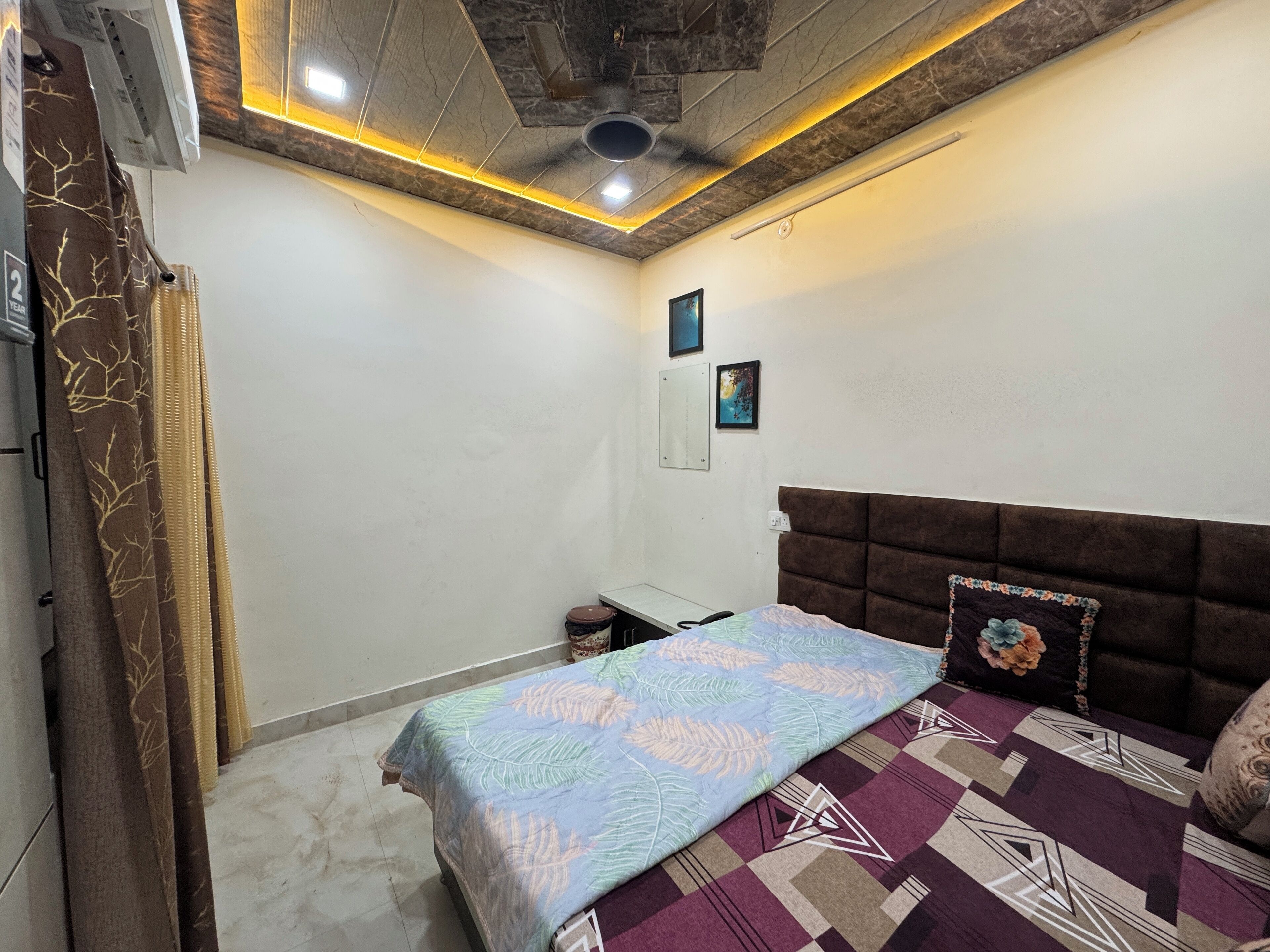 A bedroom with a bed, a nightstand, a wall-mounted air conditioner, and a ceiling fan.