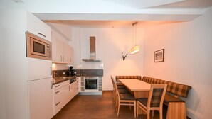 A modern kitchen with white cabinets, a built-in oven, and a dining area with a bench and chairs.