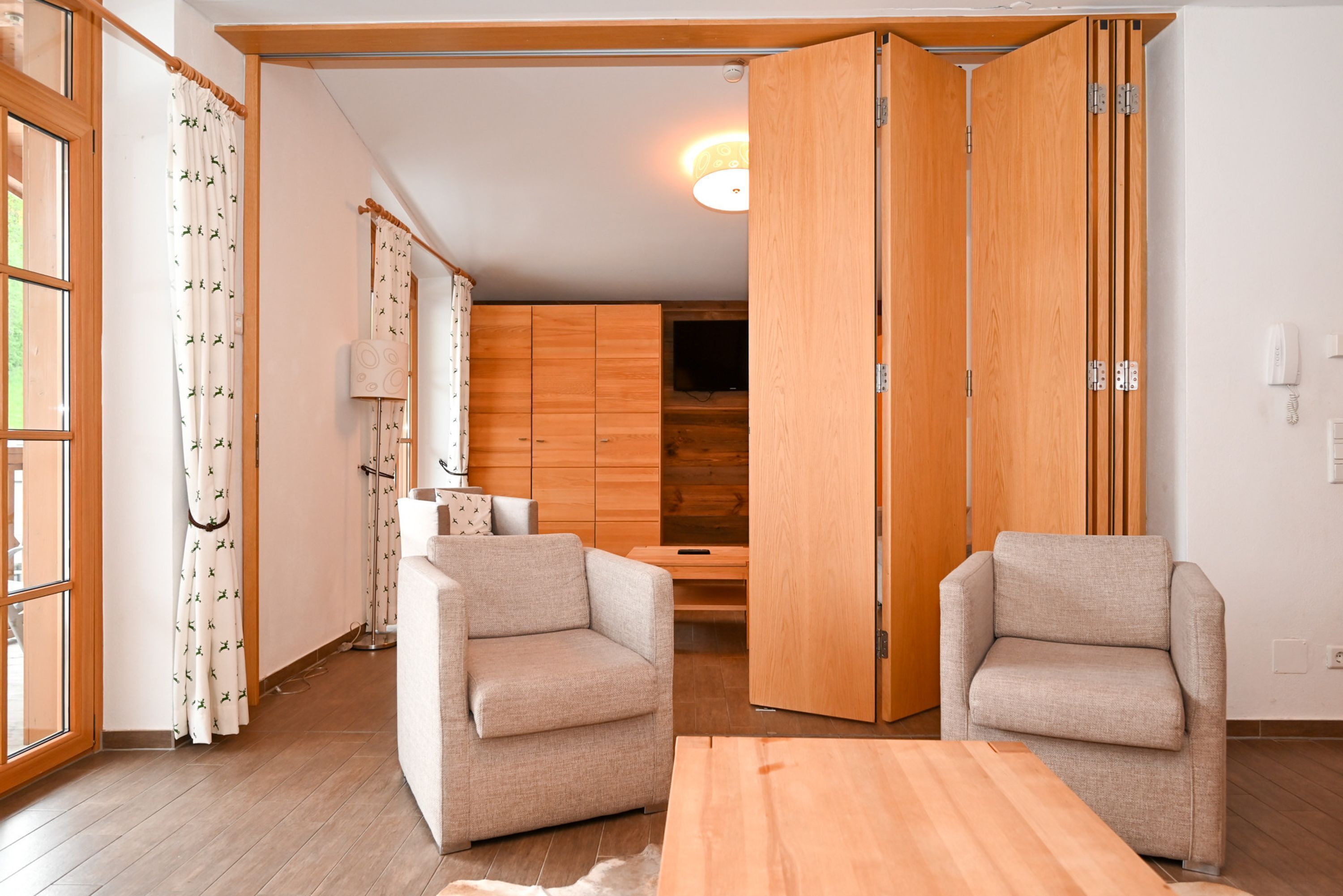 Ein modernes Wohnzimmer mit zwei beigefarbenen Sesseln, einem Holztisch und einem Holzschrank.