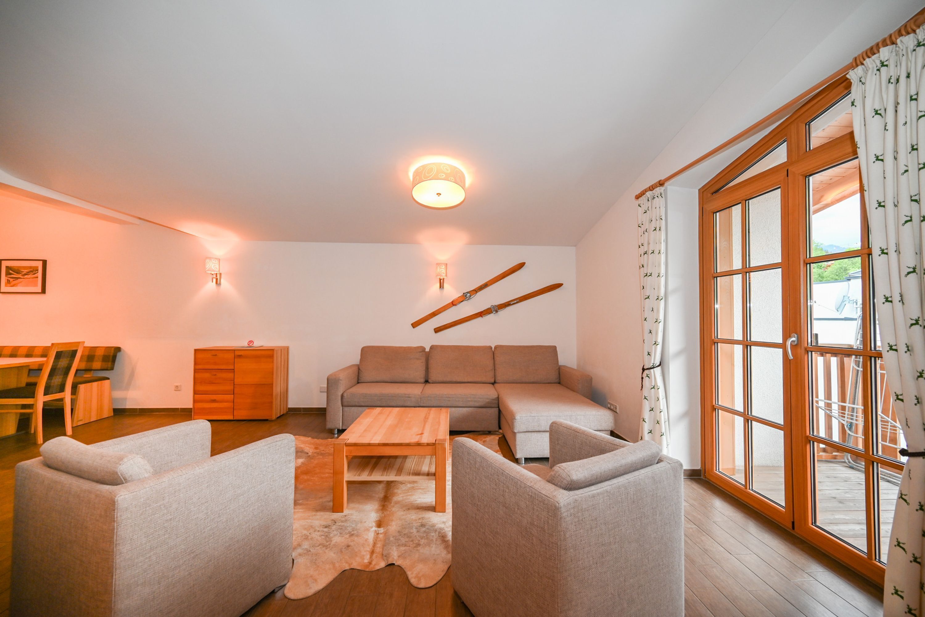 A living room with a sofa, two armchairs, a wooden coffee table, a rug, a dining table with chairs, a cabinet, and a sliding glass door with curtains.