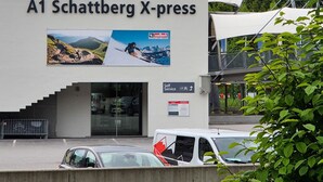 A building labeled "A1 Schattberg X-press" with a mountain view, a self-service area, and a parking lot.
