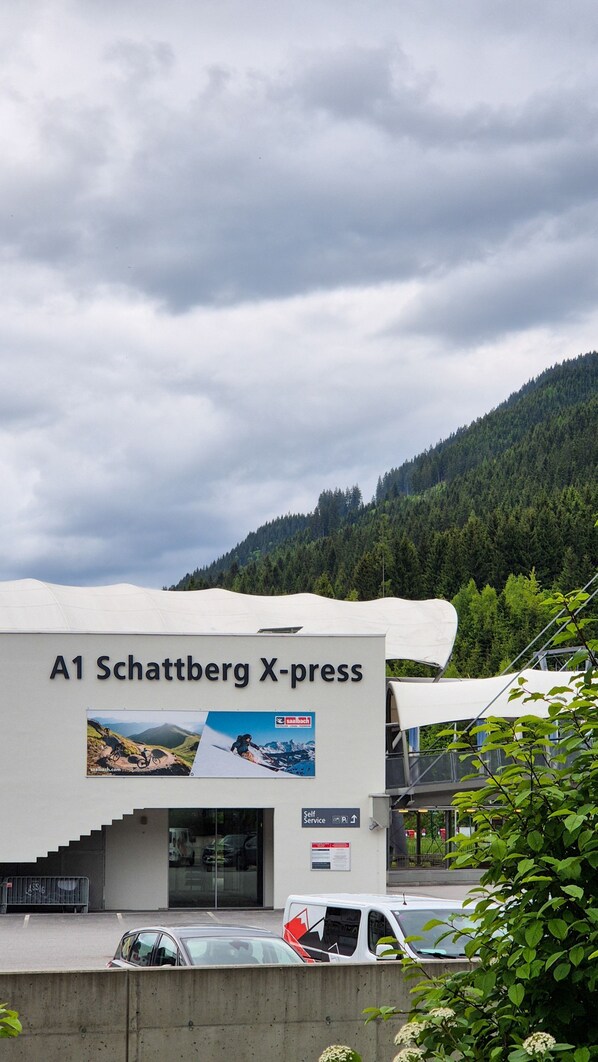 A building labeled "A1 Schattberg X-press" with a mountain view, a self-service area, and a parking lot.