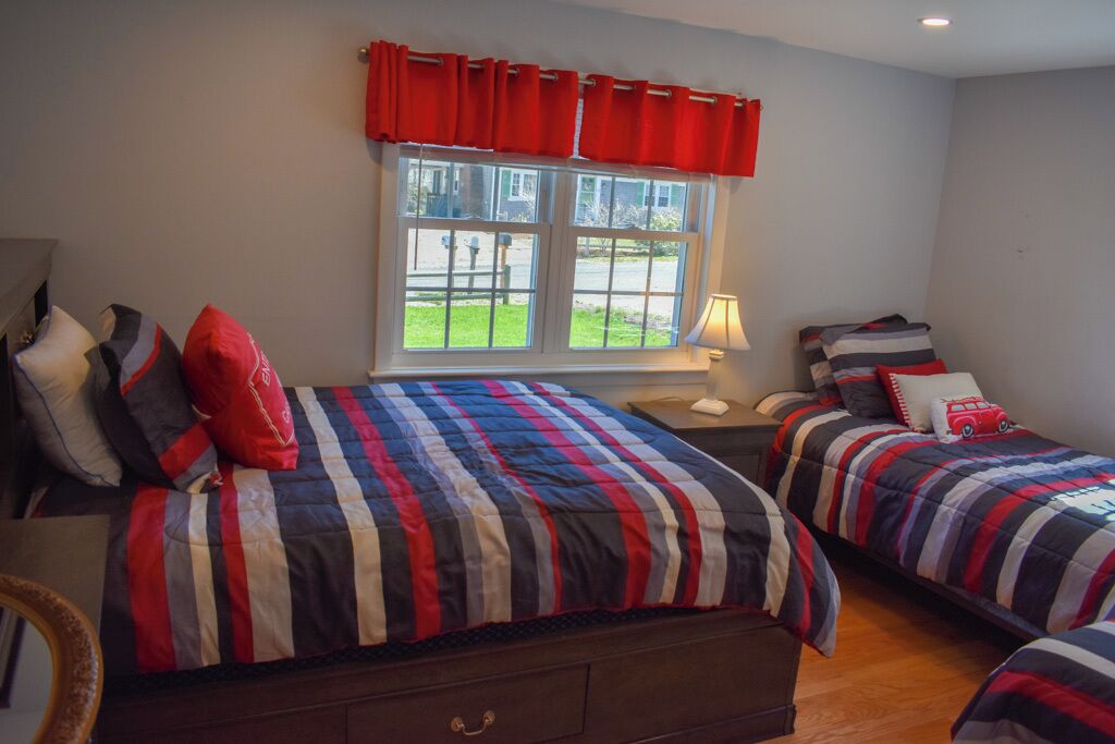 Une chambre avec deux lits, une fenêtre avec des rideaux, une lampe et une vue sur l’extérieur.