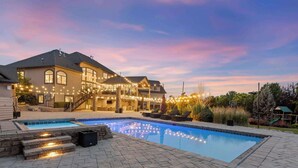A residential swimming pool area with a house, stone steps, and string lights.
