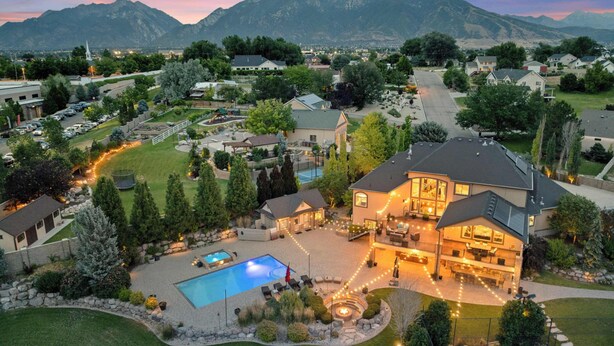 An aerial view of a residential area with a large house featuring a swimming pool, outdoor seating, and a well-maintained garden.