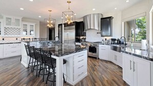A spacious kitchen with a large island, white cabinetry, stainless steel appliances, and pendant lighting.