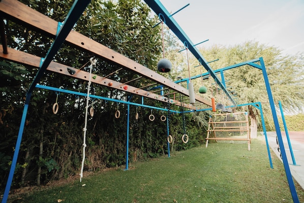 Un patio de juegos al aire libre con una estructura de madera para escalar, columpios y anillos de neumático.