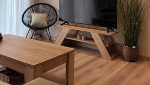 Un salon moderne avec un téléviseur à écran plat posé sur un meuble en bois, un fauteuil noir avec un coussin, une table basse en bois et une plante en pot.