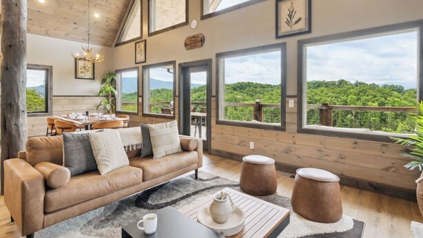 A spacious room with a large window overlooking a lush landscape, a cozy seating area with a leather couch and a coffee table, and a dining area with a wooden table and chairs.