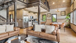 A spacious living area with a high ceiling, a wooden staircase, a kitchen with modern appliances, and a dining area with a large window.
