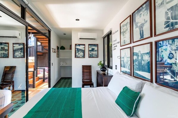 A hotel room with a bed, a desk, and a chair. There are framed pictures on the wall and a window with a view. - Cabane Container Hotel - Adults Only (Puerto Escondido)
