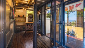 A restaurant interior with wooden flooring, a glass door leading outside, and a chalkboard menu. - Cabane Container Hotel - Adults Only (Puerto Escondido)
