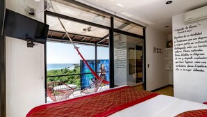 A modern hotel room with a large bed, a view of the ocean, a red hammock, and a wall with text. - Cabane Container Hotel - Adults Only (Puerto Escondido)
