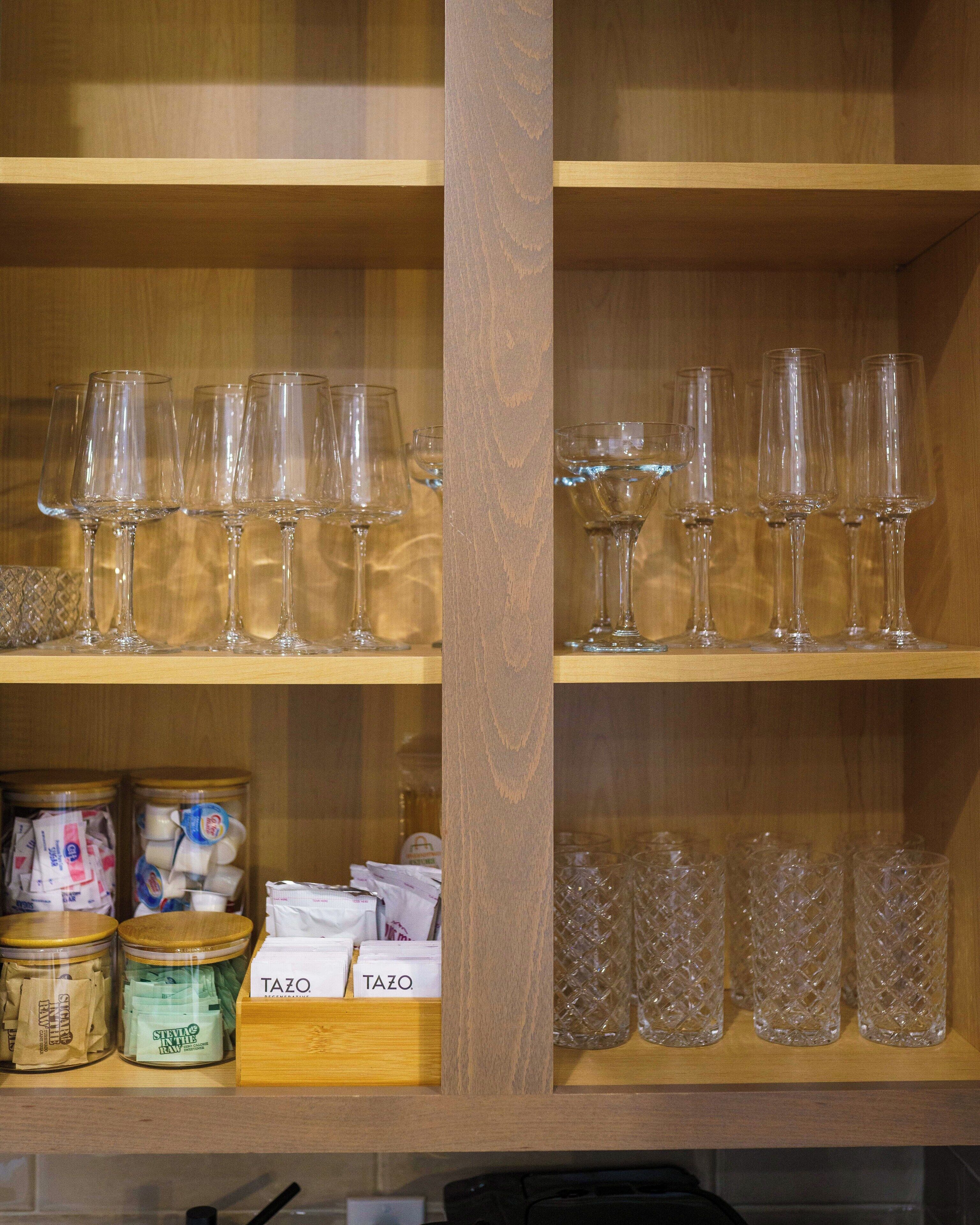 A shelf with wine glasses and jars of condiments.