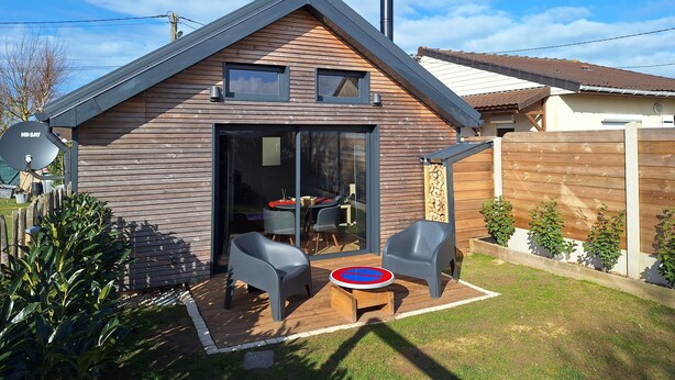 A modern house with a sloped roof, a glass door entrance, and a patio area with two chairs and a table. - Tiny house with nordic Bath, (Criel-sur-Mer)