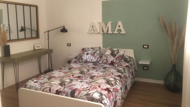 Une chambre à coucher comprenant un lit, un bureau, une lampe, un miroir fixé au mur et un panneau décoratif.