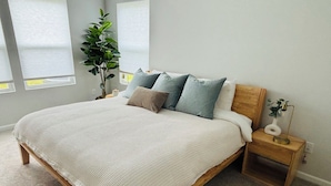 A bedroom with a large bed, a nightstand with a lamp, and a potted plant.