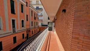 A corridor with a brick wall on one side and a railing on the other, leading to a building with multiple windows and balconies. - Vacation House Fiore Ciampino Airport - Rome Station (Ciampino)