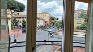 A view from a window with a metal railing, overlooking a street with buildings and a tree. - Vacation House Fiore Ciampino Airport - Rome Station (Ciampino)