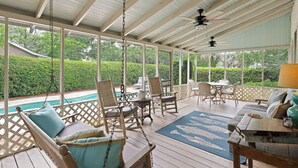 Ein überdachter Außenbereich mit Pool, Sitzgelegenheiten und Deckenventilator.