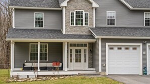 A two-story house with a stone accent wall, a covered porch with seating, and a garage.