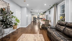 A spacious living room with a leather sofa, a dining table with chairs, and a kitchen in the background.