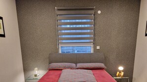 Een moderne slaapkamer met een groot bed, een raam met zonwering, een nachtkastje met een lamp en een vloerbedekking.