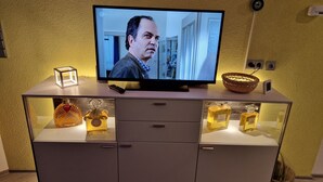 Een televisie op een kast met een afstandsbediening, een decoratieve kubus en twee parfumflesjes.