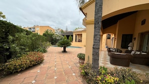 Un patio con sendero de baldosas, mobiliario exterior y abundante vegetación.