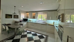Una cocina con piso a cuadros, gabinetes blancos, un fregadero y un ventanal con cortinas.