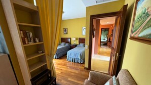 Habitación de hotel con piso de madera, un sofá, una cama con ropa de cama azul, una estantería y un cuadro en la pared.