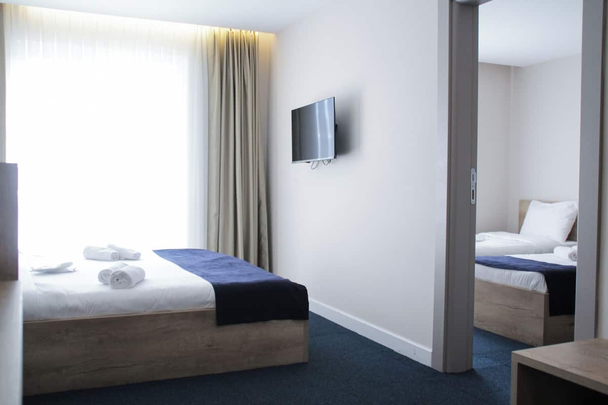 A hotel room with a bed, a TV mounted on the wall, and a window with curtains.