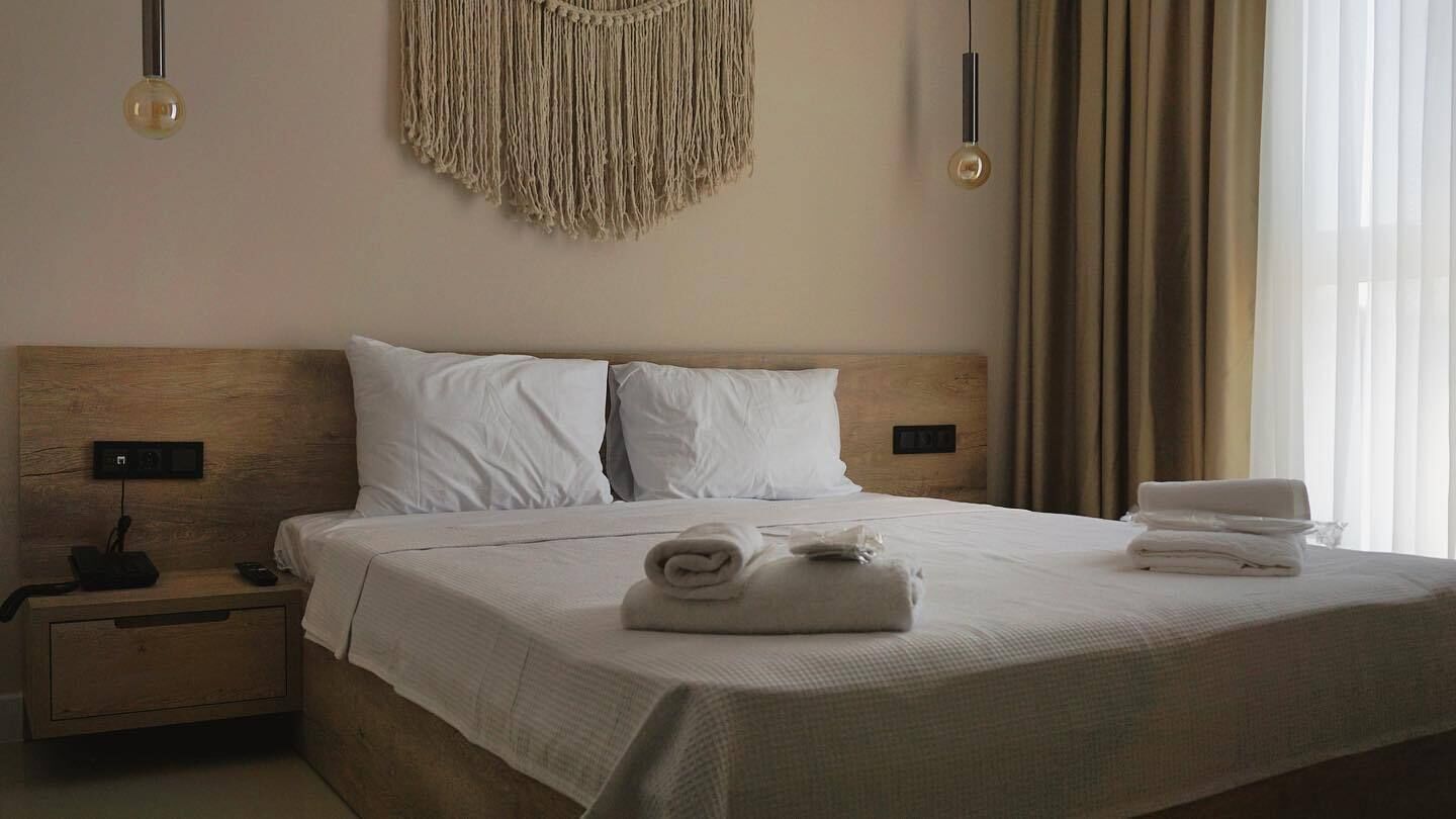 A neatly made bed with white linens, a wooden headboard, and a macrame wall hanging.