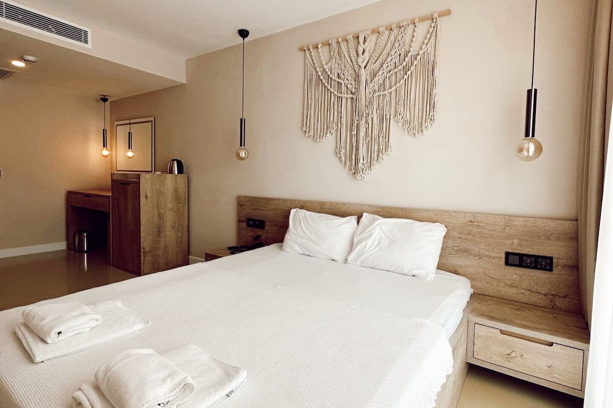 A large bed with white linens and towels, a wooden headboard, and a macrame wall hanging.