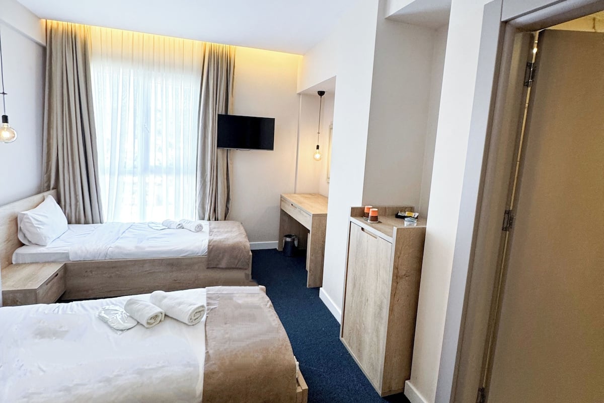 A hotel room with two beds, a desk, a TV, and a door.
