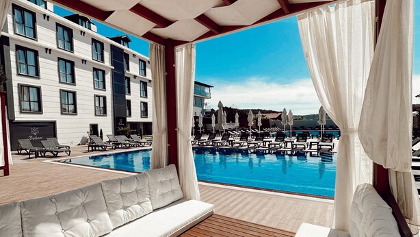 Zona junto a la piscina con cubierta de madera, asientos blancos acolchados y vistas a un puerto deportivo con barcos.