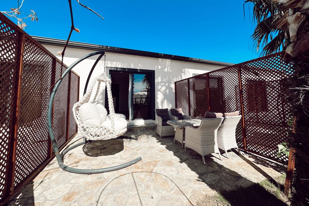 A patio with wicker furniture, a hanging chair, and a stone floor.