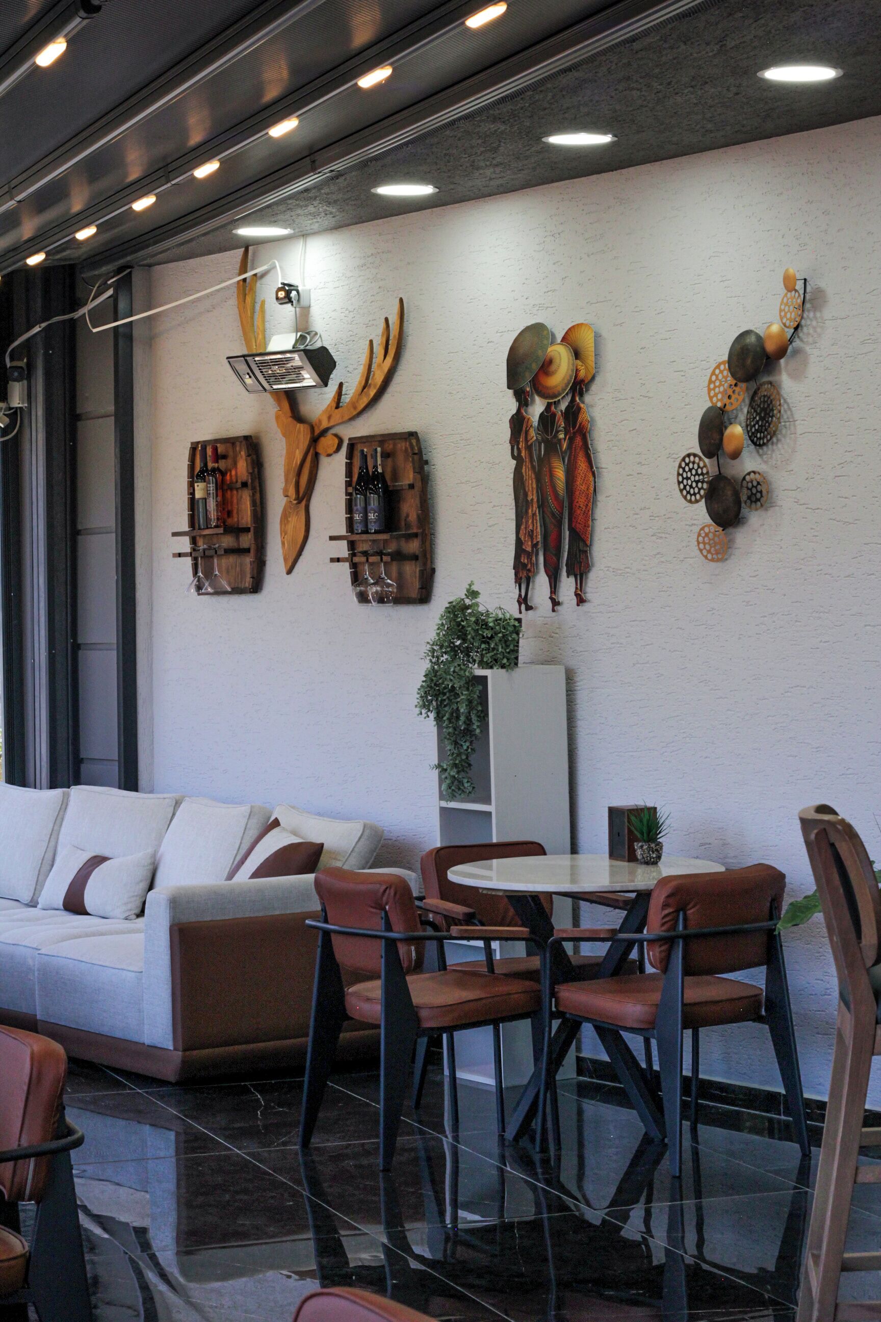 Um interior moderno com um sofá, cadeiras de jantar e uma mesa. Arte decorativa na parede inclui chifres, cabeça de veado e um padrão circular.