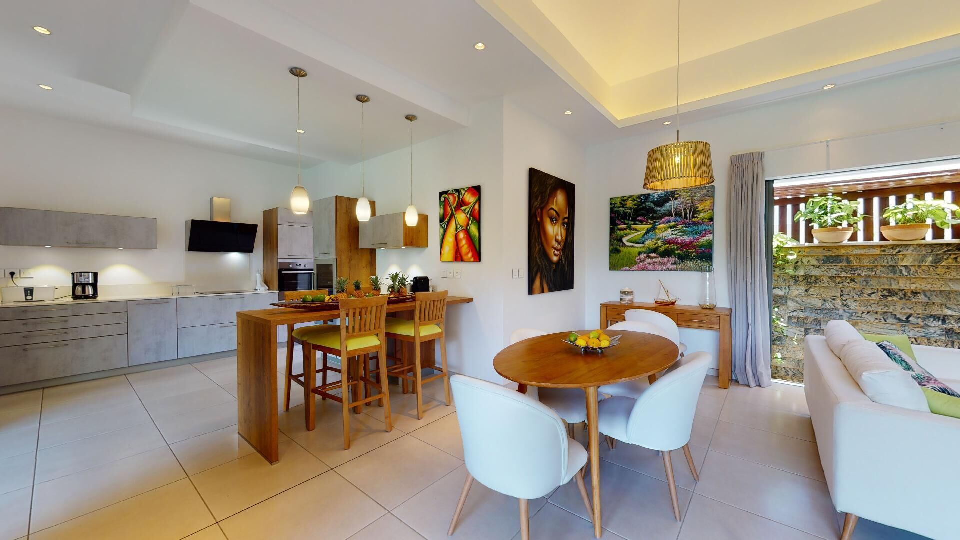 A modern kitchen with a dining area, a living room with a sofa, and a balcony with plants.