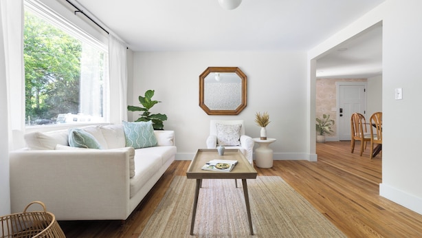 A spacious living room with a white sofa, a coffee table, and a large window. - Luxury King Suite, 125-yr historic home, 2 blocks from Main St. Crib included (Clayton)