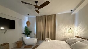 A modern bedroom with a large bed, a built-in bathtub, a ceiling fan, and a wall-mounted TV. - Ocean Park Beach Club Full (San Juan)