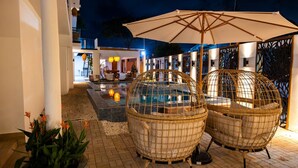 A poolside area with wicker chairs and an umbrella, a pool, and a bar area with seating. - Ocean Park Beach Club Full (San Juan)