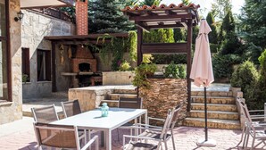 Eine Terrasse im Freien mit Kamin aus Stein, einem Tisch mit Stühlen und einer Pergola mit Sonnenschirm.