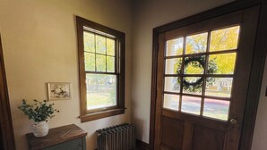 Una puerta de madera con un panel de vidrio, un radiador debajo y una mesita con una planta a la izquierda.