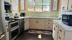 Una cocina moderna con electrodomésticos de acero inoxidable, horno empotrado, lavavajillas y microondas. Hay una ventana con persianas, un fregadero y una alfombra estampada en el suelo.